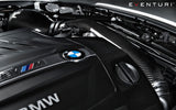 Eine Nahaufnahme eines Motorraums eines BMW M2 F87 mit Kohlefaserkomponenten zeigt deutlich das Eventuri Carbon Ansaugsystem für BMW M2 F87. Das BMW-Logo steht stolz im Vordergrund und fängt den Venturi-Effekt ein. Das Bild strahlt eine elegante, leistungsstarke Ästhetik aus und zeigt Präzisionstechnik und moderne Automobiltechnologie.